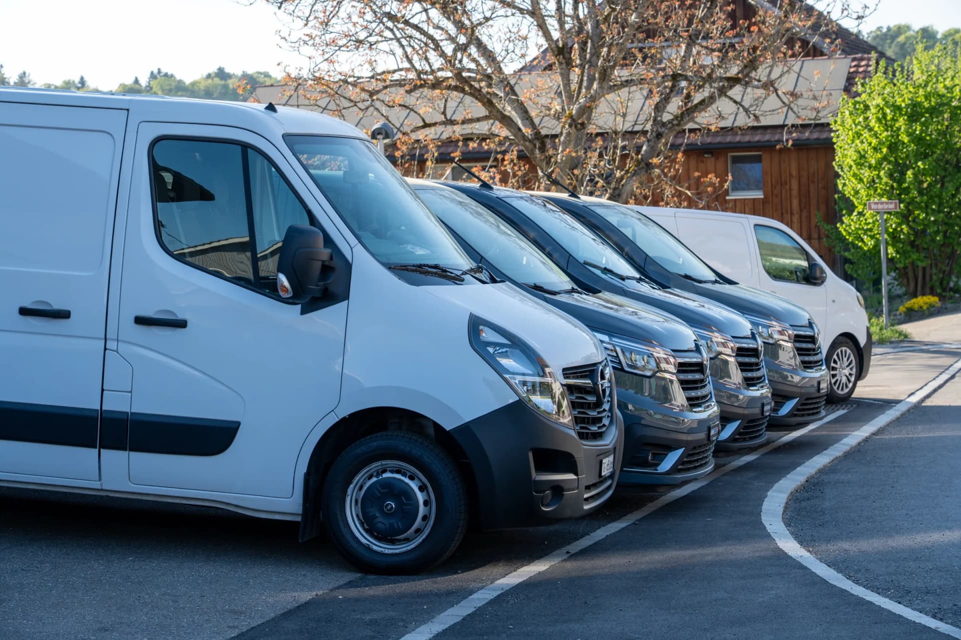 Vier Transporter stehen dicht hintereinander in einer Reihe vor der Werkstatt.